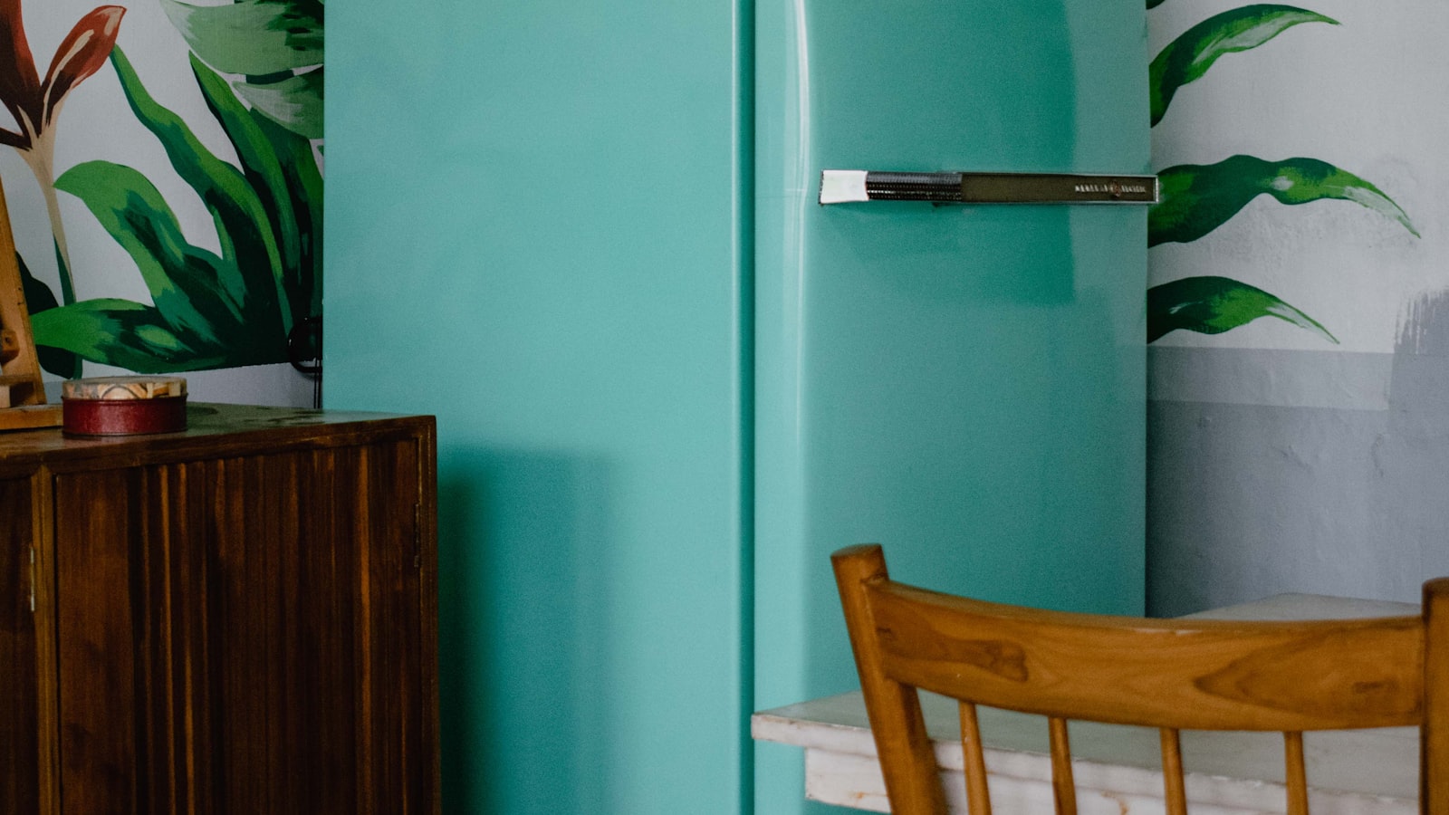 A pale teal vintage refrigerator standing in a kitchen corner beside a wooden chair.